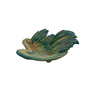 May include: A ceramic sculpture of a swan in shades of blue, green, and beige. The swan's wings are spread, and its beak is slightly open. The sculpture is on a white background.