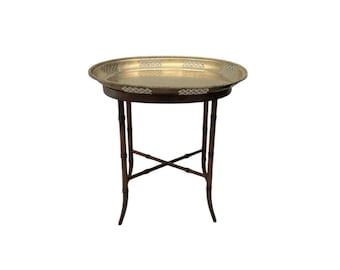 Puede incluir: Una mesa redonda de bandeja de latón con un diseño decorativo intrincado en la bandeja. La mesa tiene una base de madera marrón oscuro con cuatro patas.