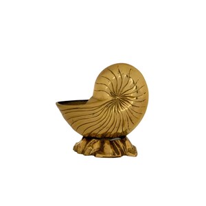 May include: A gold-colored brass nautilus shell sculpture with a detailed spiral pattern. The shell is mounted on a base.