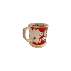May include: A white ceramic mug with a red and gold design. The mug features a handle and is decorated with red birds and blue floral accents. The rim and base have gold trim.
