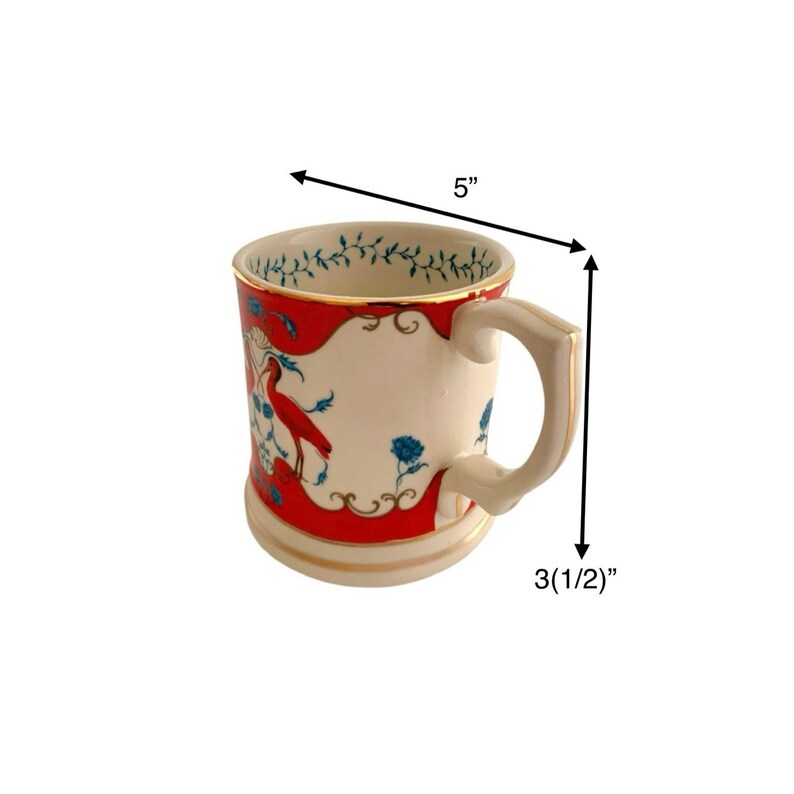 May include: Cream-colored ceramic mug with a red and blue bird and floral design. The mug has a gold rim and handle, and measures 5 inches wide and 3.5 inches tall. The interior rim features a green and white floral pattern.