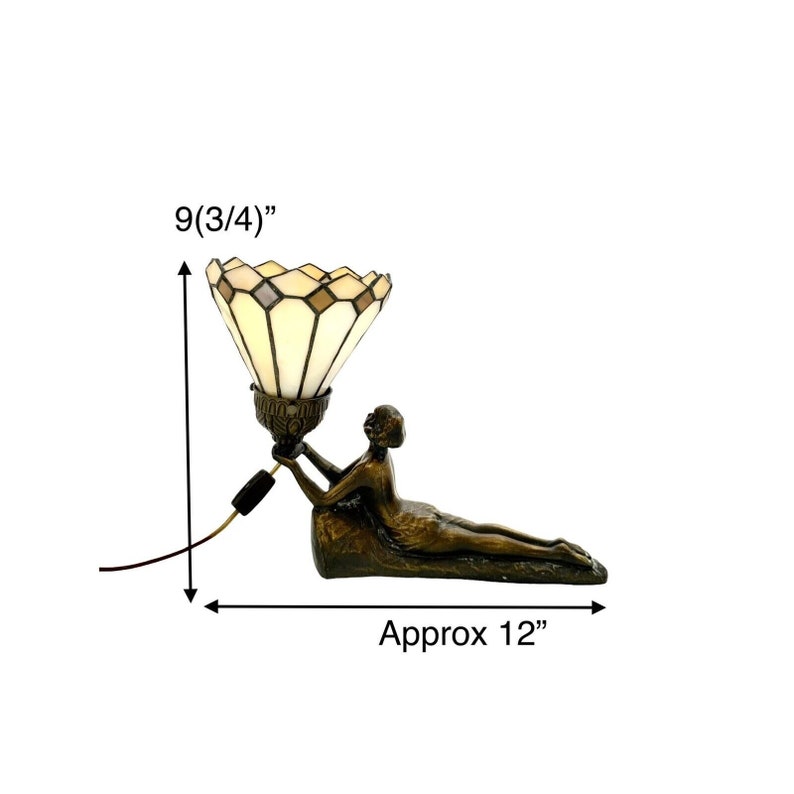 May include: A Tiffany-style lamp with a white and brown stained glass shade, held by a bronze sculpture of a woman reclining. The lamp is 9 3/4 inches tall and 12 inches wide.
