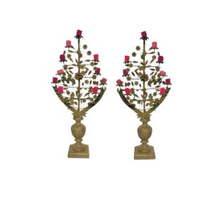 May include: A pair of gold-toned metal candle holders in the shape of a tree with pink rose-shaped candle holders. The candle holders are on a white background.