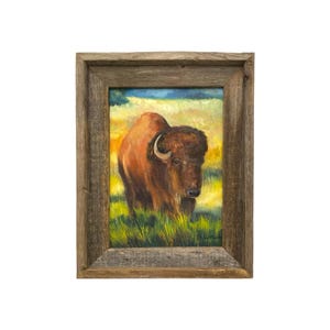 May include: A framed oil painting of a brown bison standing in a field of tall yellow and green grass. The artwork is enclosed in a rustic, weathered brown wooden frame with a visible grain texture, creating a natural border around the scene.