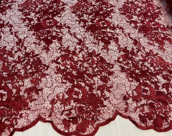 Puede incluir: Tela de encaje de color rojo burdeos con un patrón floral. El encaje tiene un diseño delicado e intrincado con pequeñas cuentas brillantes en todo.