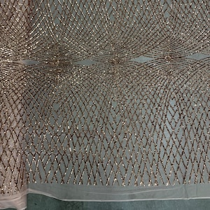 May include: A close-up of a gold glitter fabric with a geometric pattern. The fabric has a mesh backing and is perfect for adding sparkle to any project.