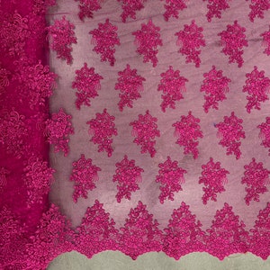 May include: Pink floral lace fabric with a delicate pattern. The lace has a scalloped edge and is perfect for adding a touch of elegance to any project.