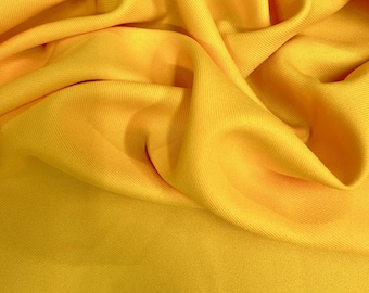 Puede incluir: Primer plano de una tela amarilla vibrante con pliegues suaves y textura sutil. El material parece ser un textil ligero, posiblemente adecuado para ropa o fines decorativos. El color es un amarillo brillante y soleado.