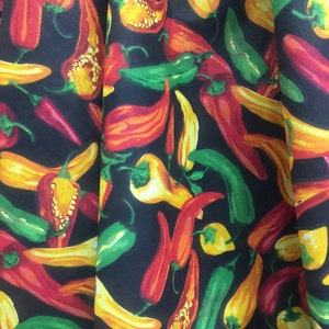 May include: A black fabric with a repeating pattern of red, yellow, and green chili peppers. The peppers are arranged in a random pattern and are all facing different directions.