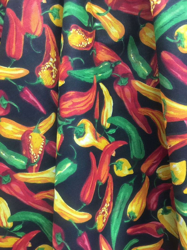 May include: A black fabric with a repeating pattern of red, yellow, and green chili peppers. The peppers are arranged in a random pattern and are all facing different directions.