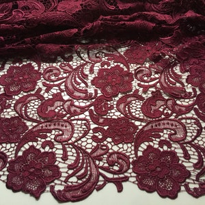 May include: Burgundy lace fabric with a floral pattern. The lace has a delicate, intricate design with small flowers and swirls.