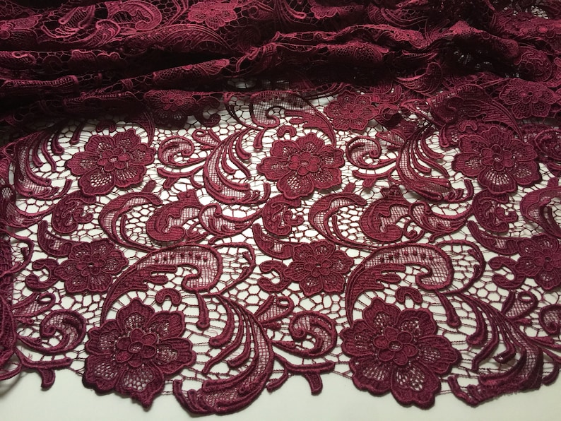 May include: Burgundy lace fabric with a floral pattern. The lace has a delicate, intricate design with small flowers and swirls.