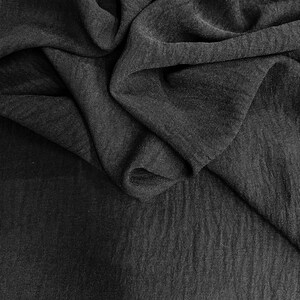 May include: A close-up shot of a dark gray fabric with a textured appearance. The fabric is draped and folded, creating shadows and highlights that emphasize its texture and depth. The material appears to be soft and flowing.