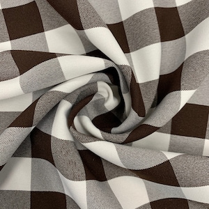 May include: Brown and white checkered fabric with a woven texture. The fabric is folded and twisted, showing the pattern and texture.