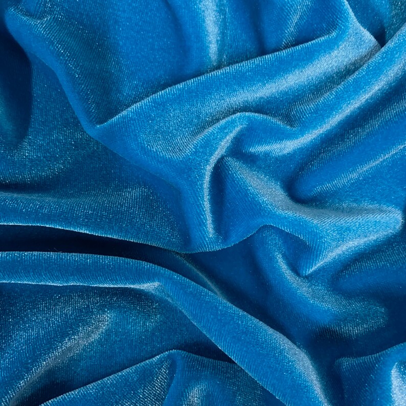 May include: Close-up of a soft, blue velvet fabric with a smooth, silky texture. The fabric is folded and draped, creating a luxurious and elegant look.