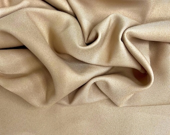 Puede incluir: Primer plano de una tela beige con textura acanalada. La tela está drapeada y doblada, creando sombras y reflejos suaves. El material parece liso y lujoso, con un brillo sutil. El efecto general es de elegancia y calidad.