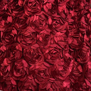 May include: Close-up of a fabric with a pattern of red roses. The roses are made of layered petals, creating a three-dimensional effect. The fabric has a dark background, and the roses are a vibrant shade of red.