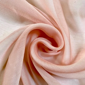 May include: A close-up of a soft, peach-colored fabric with a smooth, silky texture. The fabric is draped and folded, creating a flowing, elegant look.