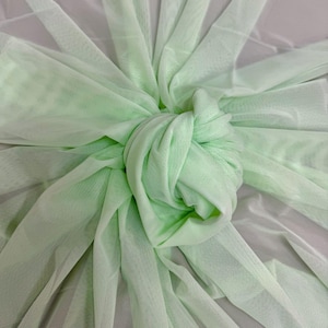 May include: Close-up of a knotted, light green fabric. The fabric is a sheer mesh material, with a knot in the center and radiating strips of fabric. The color is a soft, pastel green, and the fabric appears to be lightweight and delicate.