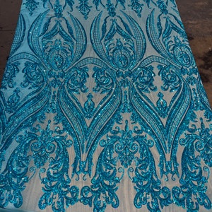 Puede incluir: Tela de lentejuelas azul turquesa con un patr&oacute;n de damasco. Las lentejuelas est&aacute;n dispersas por toda la tela, creando un efecto brillante.