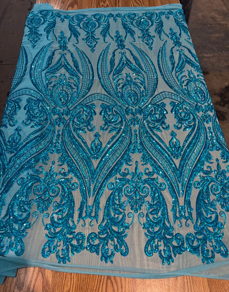 Puede incluir: Tela de lentejuelas azul turquesa con un patr&oacute;n de damasco. Las lentejuelas est&aacute;n dispersas por toda la tela, creando un efecto brillante.