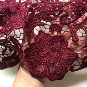 May include: Burgundy lace fabric with a floral pattern. The lace is delicate and intricate, with a soft, flowing texture.