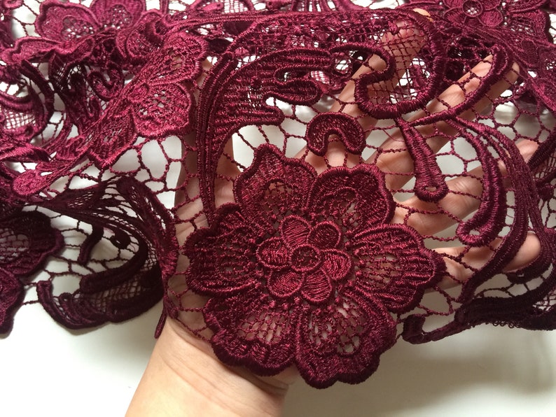 May include: Burgundy lace fabric with a floral pattern. The lace is delicate and intricate, with a soft, flowing texture.