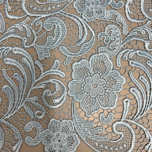 May include: Light blue lace fabric with a floral pattern. The lace features a delicate design with intricate details. The fabric is soft and lightweight, making it ideal for a variety of crafting projects.