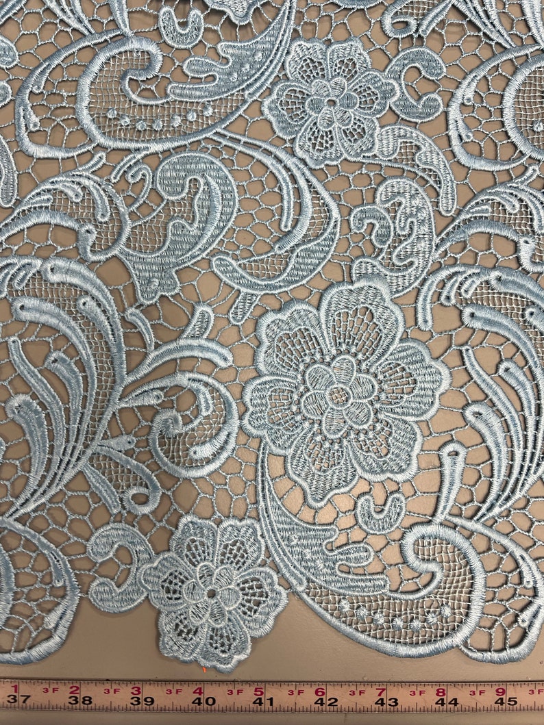 May include: Light blue lace fabric with a floral pattern. The lace features a delicate design with intricate details. The fabric is soft and lightweight, making it ideal for a variety of crafting projects.