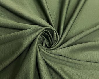 May include: Close-up of olive green fabric with a textured, woven appearance. The fabric is gathered and swirled, creating a spiral pattern in the center. The material has a slight sheen, and the folds create shadows.