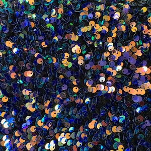 May include: A close-up of a fabric covered in iridescent sequins. The sequins are in shades of blue, green, gold, and purple.