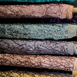 May include: Close-up of six rolls of sparkly fabric with a geometric pattern. The fabric is in various colors, including teal, pink, purple, gray, copper, and gold.