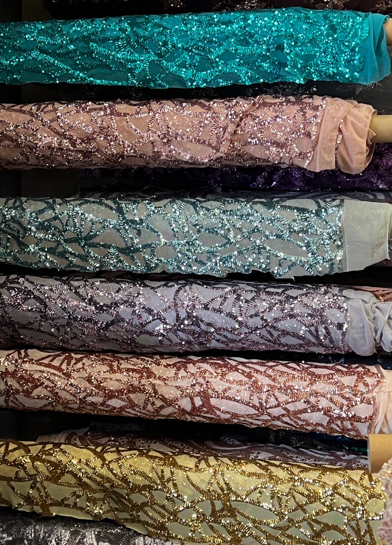 May include: Close-up of six rolls of sparkly fabric with a geometric pattern. The fabric is in various colors, including teal, pink, purple, gray, copper, and gold.