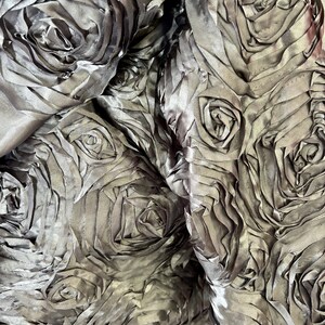 May include: A close-up of a silver fabric with a 3D rose pattern. The fabric is soft and has a subtle sheen.
