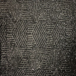 May include: Black fabric with a geometric pattern of silver glitter. The pattern is made up of overlapping diamonds and lines.