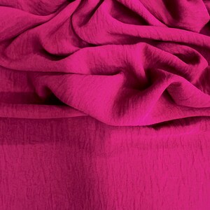 May include: A close-up shot of a vibrant fuchsia fabric with a textured, crinkled appearance. The fabric is draped in soft folds, creating shadows and highlights that emphasize its texture. The color is a rich, saturated pink.