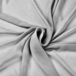 May include: A close-up of a smooth, light gray fabric with a soft, flowing texture. The fabric is draped and folded, creating a sense of movement and fluidity.