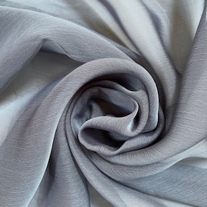 May include: Close-up of a soft, gray sheer fabric with a silky texture. The fabric is draped and folded, creating a smooth, flowing look.