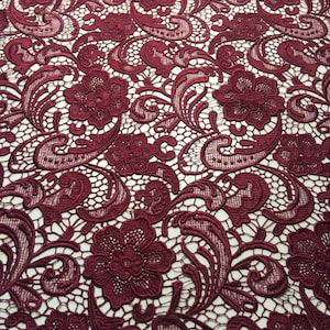 May include: Burgundy lace fabric with a floral pattern. The lace has a delicate, intricate design with small flowers and leaves.