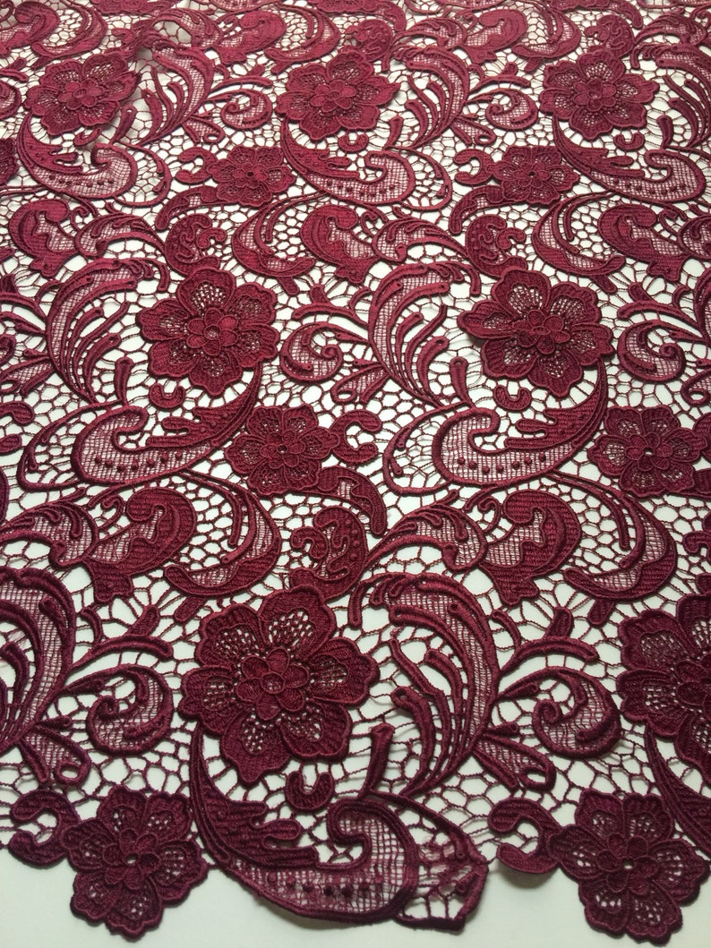 May include: Burgundy lace fabric with a floral pattern. The lace has a delicate, intricate design with small flowers and leaves.
