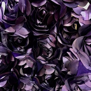 May include: Close-up of a fabric with a purple, 3D floral design. The fabric is made of many layers of petals, creating a textured and dimensional look.