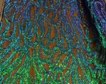 May include: Green and blue iridescent sequins on a black mesh fabric. The sequins are arranged in a swirling pattern.