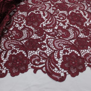 May include: Burgundy lace fabric with a floral and paisley pattern. The lace has a delicate, intricate design.