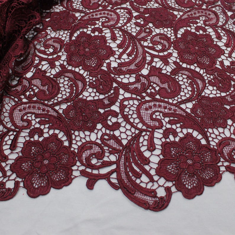 May include: Burgundy lace fabric with a floral and paisley pattern. The lace has a delicate, intricate design.