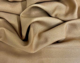 Puede incluir: Primer plano de una tela de color beige con una sutil textura acanalada. La tela está drapeada, creando pliegues y sombras suaves. El color es un tono cálido y neutro, adecuado para diversos proyectos de ropa o decoración del hogar.