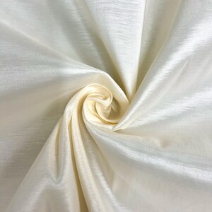 Puede incluir: Tela de color crema con un brillo sedoso. La tela está drapeada y doblada para mostrar su textura.