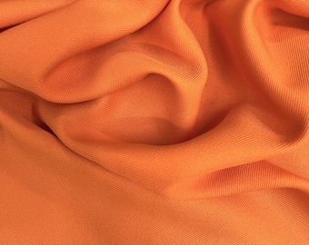 Puede incluir: Primer plano de una vibrante tela naranja con textura acanalada. El material está drapeado, creando pliegues y sombras suaves. El color es un naranja brillante y sólido, que llena el marco.
