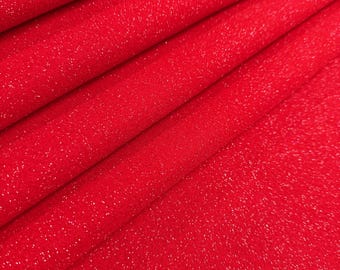 May include: Close-up of a vibrant red fabric with a subtle glitter effect. The material is folded, creating diagonal lines and shadows that add depth. The texture appears soft and slightly textured, catching the light and creating a shimmering appearance.