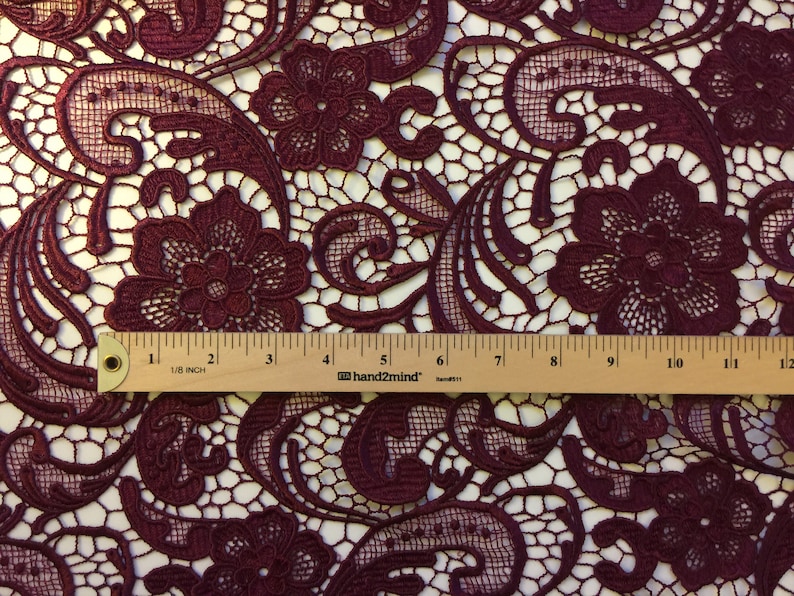 May include: Burgundy lace fabric with a floral pattern. The fabric is measured with a ruler that shows 12 inches.