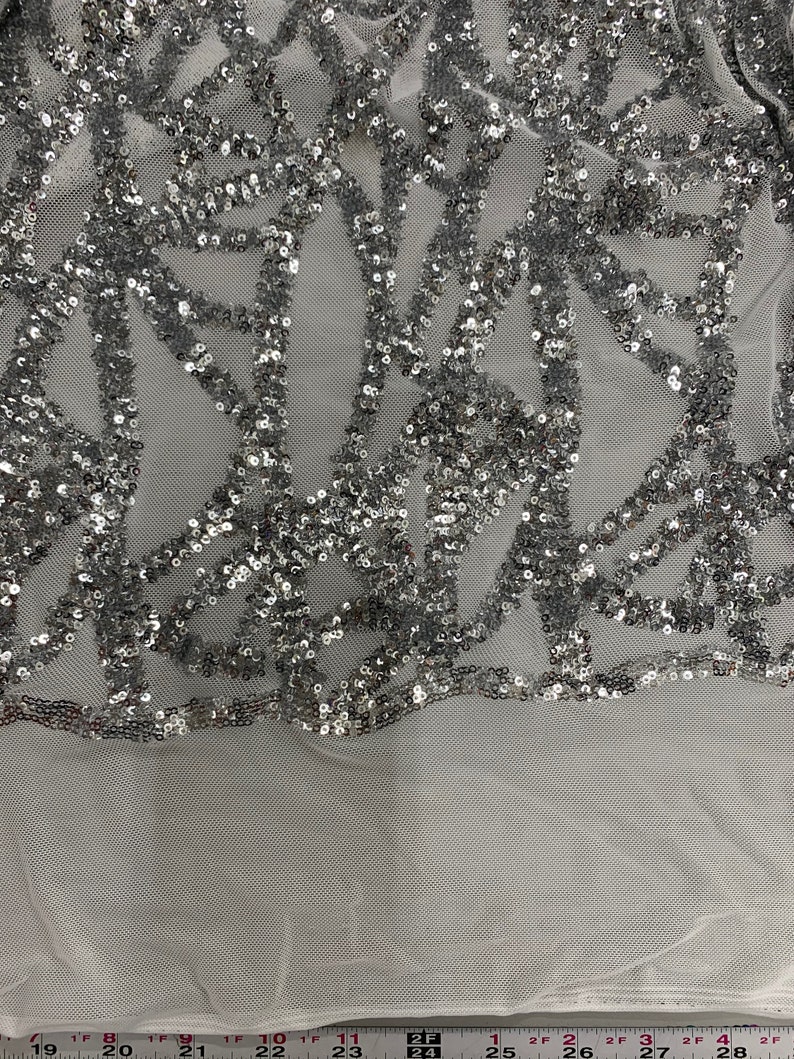 May include: Silver sequined fabric with a geometric pattern on a white mesh background.
